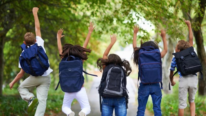 Rear-view of five children jumping in the air wearing backpacks