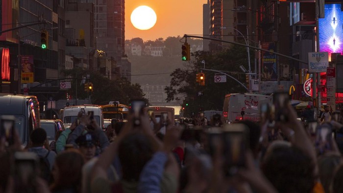 Para Pemburu Cahaya Emas Manhattanhenge di New York NEW YORK, NY - MAY 30: People stand on 42nd Street in Times Square as they photograph the second evening of the Manhattanhenge sunset on May 30, 2023, in New York City. (Photo by Gary Hershorn/Getty Images)