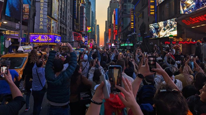 NEW YORK, NY - MAY 30:  People stand on 42nd Street in Times Square as they photograph the second evening of the Manhattanhenge sunset on May 30, 2023, in New York City.  (Photo by Gary Hershorn/Getty Images)