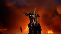 Seorang pendemo dengan pakaian tradisional Suku Guarani Mbya berdiri di kepulan asap dari ban yang dibakar.  