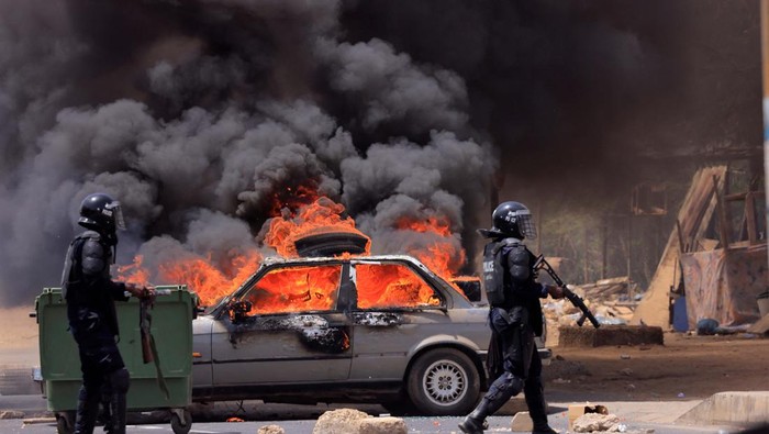 Riot police officers walk near a car set on fire during clashes between supporters of Senegalese opposition leader Ousmane Sonko and security forces after Sonko was sentenced to prison in Dakar Senegal June 1, 2023 REUTERS/Zohra Bensemra