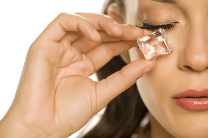 young beautiful woman holding ice cube under the eye on white background