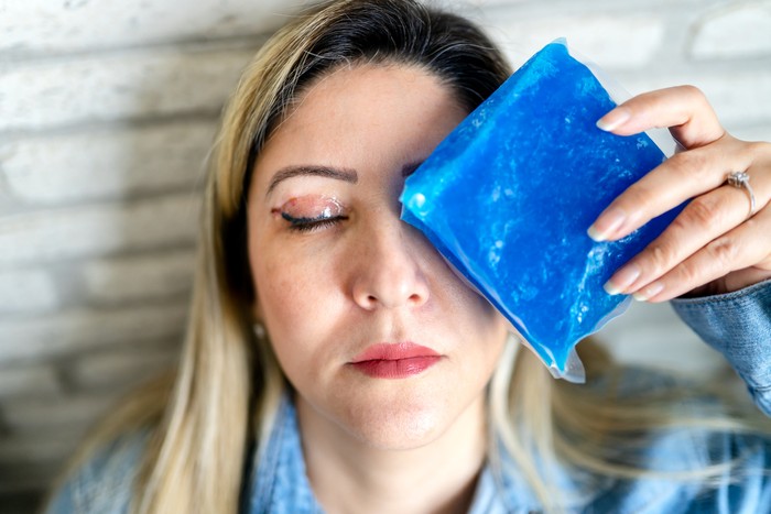 Woman having eyelid surgery applies ice compress to her face