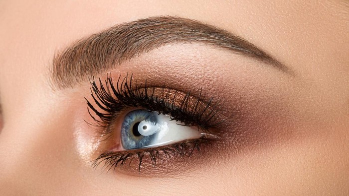 Close up of blue woman eye with beautiful brown with red and orange shades smokey eyes makeup. Modern fashion make up.