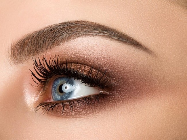 Close up of blue woman eye with beautiful brown with red and orange shades smokey eyes makeup. Modern fashion make up.
