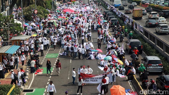 Ada Demo Nakes, Jalan Gatot Subroto Depan DPR Macet Jalan Gatot Subroto tepatnya di depan Gedung dPR/MPR terpantau padat merayap, Senin (6/6/2023). Penyebabnya yakni aksi tenaga kesehatan menuntut pembahasan RUU Kesehatan Omnibus Law dihentikan. Petugas sempat memblokir jalan dan mengalihkan arus lalu lintas dqri arah Semanggi memutar ke arah TVRI. Namun sekitar pukul 10.00 WIB, pengalihan arus dihentikan, kendaraan bisa melintas depan DPR namun hanya menyisakan satu jalur yakni jalur busway. Hingga pikul 10.26 wib, aksi masih berlangsung.