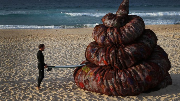 SYDNEY, AUSTRALIA - JUNE 05: A surfer interacts with a sculpture titled 'Plastic pile of sh!t, 2023' presented by Better Packaging Co. at Bondi Beach on June 05, 2023 in Sydney, Australia. The four-metre-high sculpture is made out of recycled plastic and resembles human feces. The sculpture is designed to draw attention to the amount of plastic that's dumped in the world's oceans every 30 seconds. (Photo by Lisa Maree Williams/Getty Images)