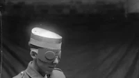 Topi Baja Dan Belati Tangan: Seorang pria memperagakan topi baja berpadu dengan kacamata dan sarung tangan belati baja sebagai pelindung dan pertahanan diri, diproduksi untuk militer Inggris selama Perang Dunia I. Foto: Wikimedia Commons