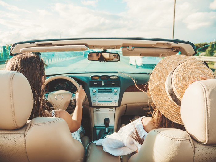 Portrait of two young beautiful and smiling hipster female in convertible car. Sexy carefree women driving cabriolet. Positive models riding and having fun in sunglasses outdoors.Enjoying summer days