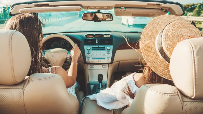 Portrait of two young beautiful and smiling hipster female in convertible car. Sexy carefree women driving cabriolet. Positive models riding and having fun in sunglasses outdoors.Enjoying summer days