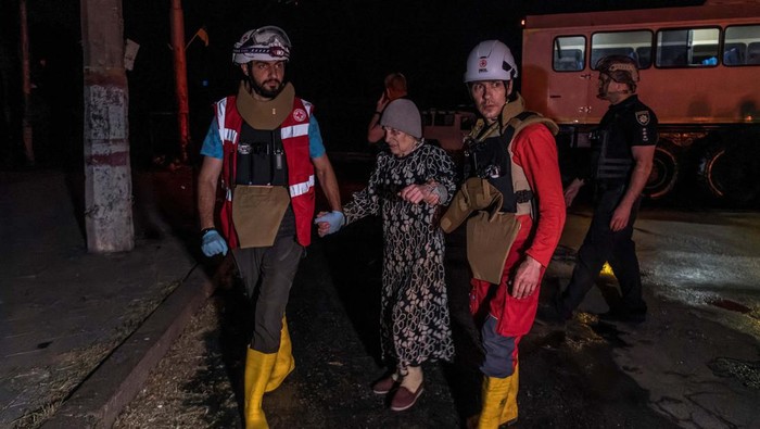 Puluhan Ribua Warga Dievakuasi Akibat Jebolnya Bendungan Kakhovka Red Cross volunteers help an elderly woman evacuated from a flooded area after the Nova Kakhovka dam breached, amid Russia's attack on Ukraine, in Kherson, Ukraine June 6, 2023. REUTERS/Ivan Antypenko