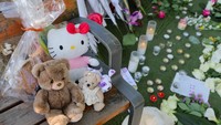 Pemandangan mainan, bunga, dan lilin yang ditinggalkan di taman Le Paquier.