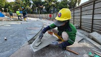 Kini, pekerja mengganti ubin lama pelataan air mancur dengan ubin baru.   