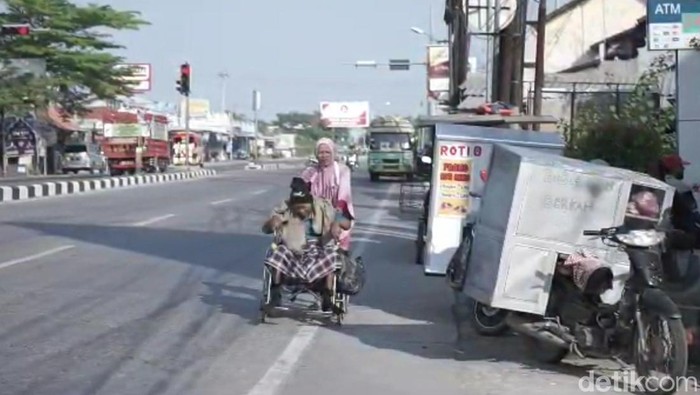 Aan, warga Brebes terpaksa mendorong kursi roda bawa suami ke RS untuk berobat.