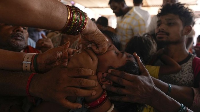 Volunteers try to open the mouth of a child suffering from asthma to administer a traditional fish medicine in Hyderabad, India, Friday, June 9, 2023. Every year thousands of asthma patients arrive here to receive this fish therapy from the Bathini Goud family, a secret formula of herbs, handed down by generations only to family members. The herbs are inserted in the mouth of a live sardine, or murrel fish, and slipped into the patient's throat. (AP Photo/Mahesh Kumar A.)