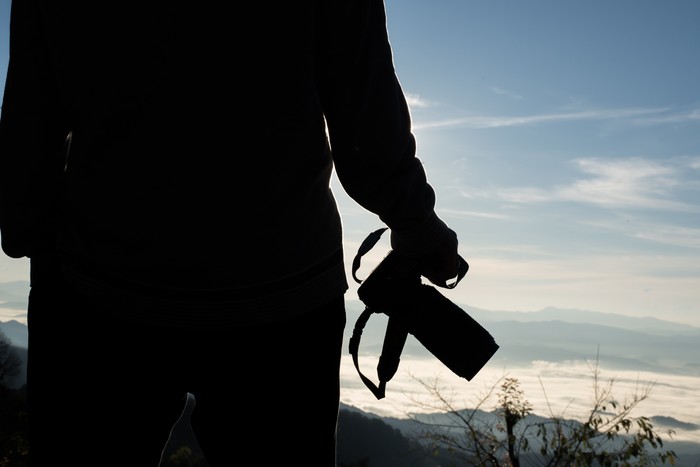 Silhouette  young photographer holding a camera with landscape in the mountain.