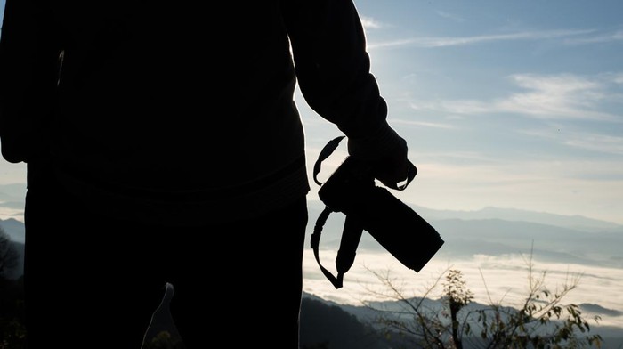 Silhouette  young photographer holding a camera with landscape in the mountain.