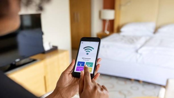 Over the shoulder view of businesswoman connecting to the mobile wifi in hotel room. Wifi icon on mobile phone display.