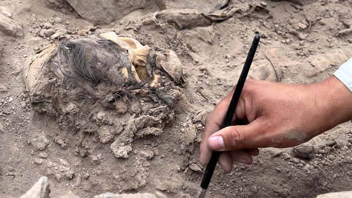 An archaeologist works at the excavation site of a pre-Hispanic burial next to a mummy believed to be from the Manchay culture, which developed in the valleys of Lima between 1,500 and 1,000 BCE, in Lima, Peru, June 14, 2023. REUTERS/Anthony Marina NO RESALES. NO ARCHIVES