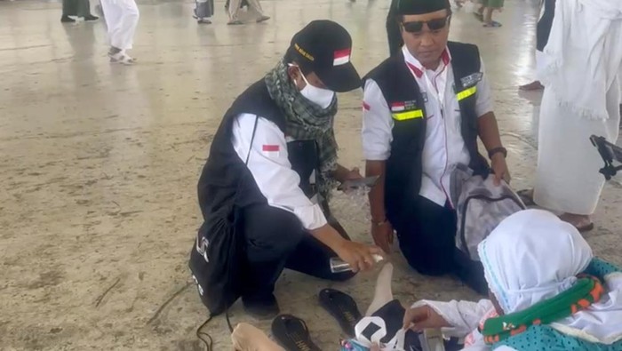 Petugas  tengah memasangkan sandal kepada jemaah haji Indonesia