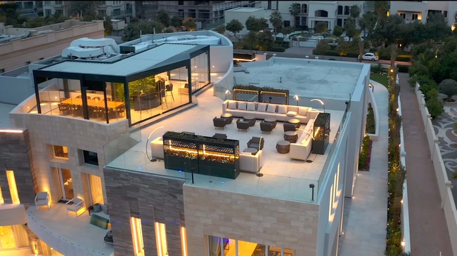 Rumah mewah tak lengkap rasanya jika tak memiliki rooftop. Pada area rooftop ada ruangan indoor dan outdoor yang luas. Area indoor yang dindingnya kaca dilengkapi dengan bar, sedangkan outdoor memiliki desain seamless dan pemandangan gedung-gedung pencakar langit Dubai. Foto: Dok. YouTube Luxe List