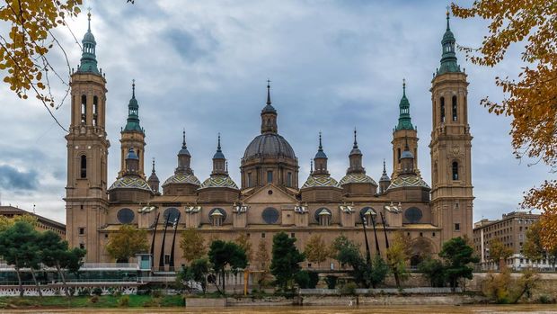 Cathedral-Basilica of Our Lady of the Pillar on the embankment of Ebro river with yellow water in Zaragoza on an autumn day, Spain. Panoramic view of the Spanish Roman Catholic Church