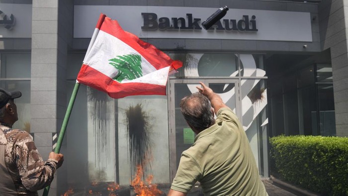 A protester throws a bottle of oil at the windows of Bank Audi during a protest demanding the release of depositors trapped savings, in Beirut, Lebanon, Thursday, June 15, 2023. Since Lebanon fell into a financial crisis in 2019, the banks have imposed informal capital controls, restricting depositors from accessing their funds, while the countrys currency has collapsed and inflation has spiraled. (AP Photo/Hussein Malla)