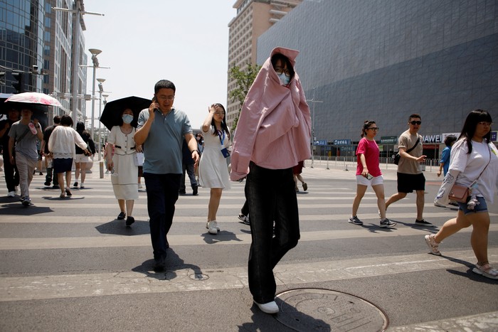A pedestrian shields herself from the sun as she crosses a road on a hot day amid an orange alert for heatwave, in Beijing, China June 16, 2023. REUTERS/Florence Lo