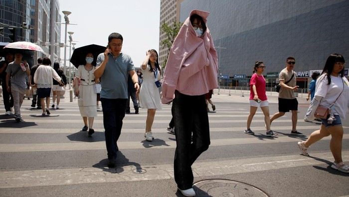 A pedestrian shields herself from the sun as she crosses a road on a hot day amid an orange alert for heatwave, in Beijing, China June 16, 2023. REUTERS/Florence Lo