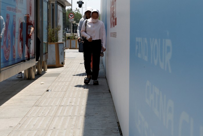 A pedestrian shields herself from the sun as she crosses a road on a hot day amid an orange alert for heatwave, in Beijing, China June 16, 2023. REUTERS/Florence Lo