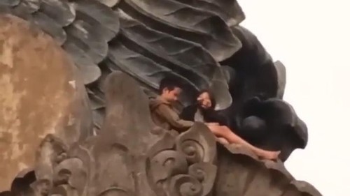 Tangkapan layar dua remaja yang duduk di atas patung Garuda Wisnu Serasi (GWS) Tabanan, Bali.