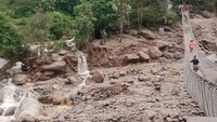 Orang-orang berjalan di atas jembatan dekat lokasi longsor akibat hujan lebat. Rekaman video yang diambil oleh seorang saksi mata menunjukkan akibatnya berupa lumpur dan bebatuan di sepanjang Sungai Hewa yang mengamuk di dekat pembangkit listrik tenaga air yang rusak.