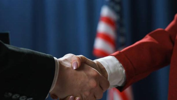 Close-up of a handshake of a man and a woman politicians on a blue background with a US flag