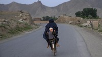 Seorang pria membonceng seorang anak di belakang sepeda di provinsi Wardak, Afghanistan, Minggu (18/6/2023). (AP Photo/Ebrahim Noroozi)