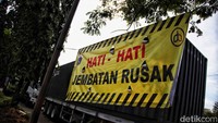 Sebuah spanduk yang meminta pengendara hati-hati karena ada jembatan rusak terpampang di sekitar lokasi. 