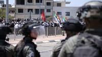 Polisi Israel dengan perlengkapan anti huru hara berdiri di dekat pengunjuk rasa Druze ketika ribuan orang mengambil bagian dalam demonstrasi menentang pembangunan turbin angin besar-besaran di Dataran Tinggi Golan, Rabu (21/6/2023). Polisi Israel menembakkan gas air mata, peluru berujung spons, dan meriam air selama demonstrasi massa oleh Druze Arab. AP/Fadi Amun  