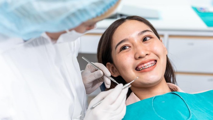 Orthodontist doctor examine tooth to woman patient at dental clinic. Attractive young girl with braces lying on dental chair, getting dental treatment from dentist during procedure service in hospital