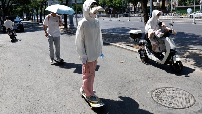 People shield themselves from the sun, as they walk amid a red alert for heatwave in Beijing, China June 23, 2023. REUTERS/Tingshu Wang
