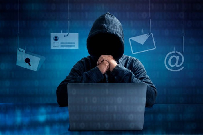 Hacker in hoodie dark theme Hacker in a blue hoody standing in front of a coding background with binary streams and information security terms cybersecurity concept