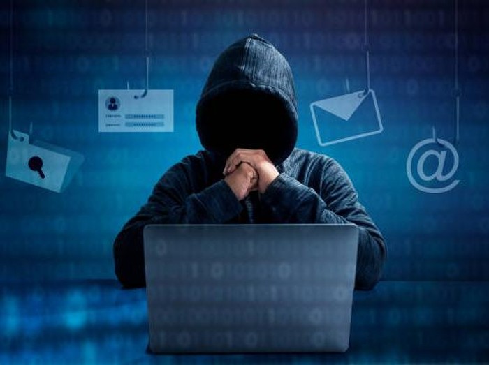 Hacker in hoodie dark theme Hacker in a blue hoody standing in front of a coding background with binary streams and information security terms cybersecurity concept