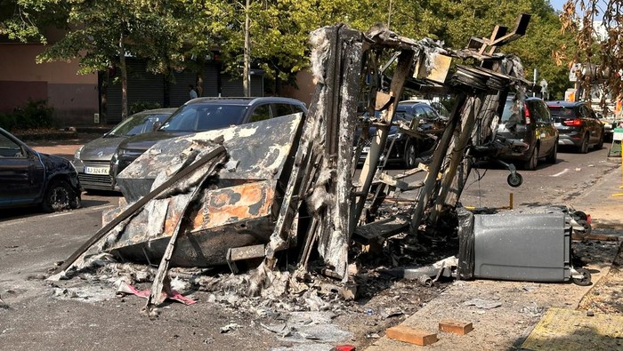 FRANCE-SECURITY/PARIS A woman walks in a street past a car, burnt during clashes between youths and police, the day after the death of a 17-year-old teenager killed by a French police officer during a traffic stop, in Nanterre, Paris suburb, France, June 28, 2023. REUTERS/Gonzalo Fuentes
