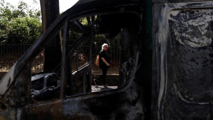 FRANCE-SECURITY/PARIS A woman walks in a street past a car, burnt during clashes between youths and police, the day after the death of a 17-year-old teenager killed by a French police officer during a traffic stop, in Nanterre, Paris suburb, France, June 28, 2023. REUTERS/Gonzalo Fuentes
