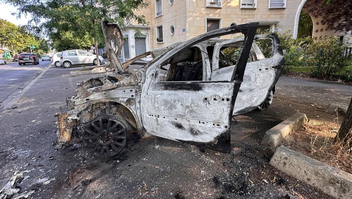 FRANCE-SECURITY/PARIS A woman walks in a street past a car, burnt during clashes between youths and police, the day after the death of a 17-year-old teenager killed by a French police officer during a traffic stop, in Nanterre, Paris suburb, France, June 28, 2023. REUTERS/Gonzalo Fuentes