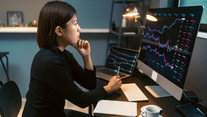 A young woman is doing cryptocurrency business trading on her computer at home at nigh.