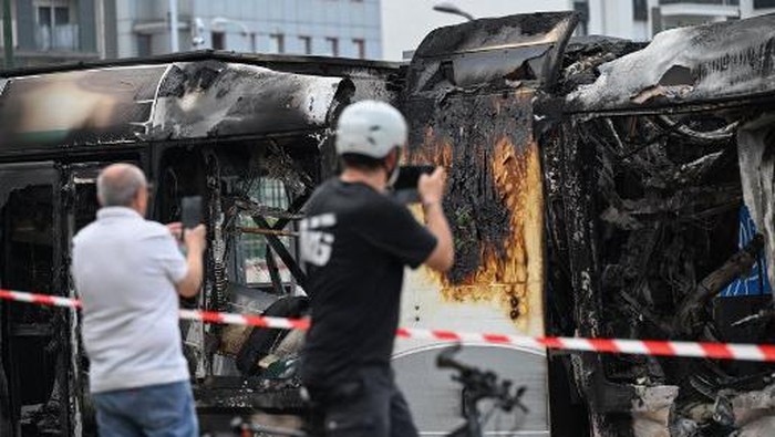 People photograph a burnt tram destroyed during protests the previous night, in Clamart, southwestern Paris, on June 29, 2023. Protests erupted across the greater Paris region that saw protesters burn cars, lorries and trams in reaction to the shooting by police of a 17-year-old boy at point-blank range on June 27, 2023, in Nanterre, Paris, in an incident that has reignited debate in France about police tactics long criticised by rights groups over the treatment of people in low-income suburbs, particularly ethnic minorities. (Photo by Emmanuel DUNAND / AFP)