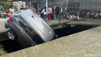 Seorang juru parkir menyebut sopir mobil yang hendak berputar arah ini tak mendengar instruksi untuk stop sehingga mobil masuk ke dalam kali.