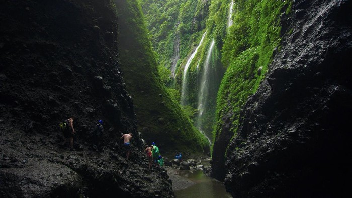 Wisatawan berjalan di bebatuan saat mengunjungi Air Terjun Madakaripura di Probolinggo, Jawa Timur, Jumat (30/6/2023). Pada libur Idul Adha, kunjungan wisatawan di air terjun tersebut meningkat hingga 100 pengunjung per hari dibanding hari biasa yang hanya mencapai 36 orang per hari. ANTARA FOTO/Irfan Sumanjaya/rwa.