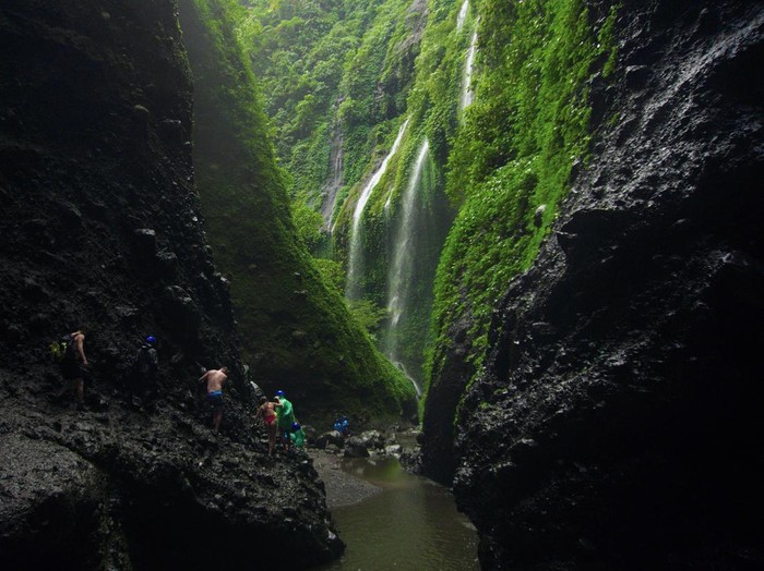 Wisatawan berjalan di bebatuan saat mengunjungi Air Terjun Madakaripura di Probolinggo, Jawa Timur, Jumat (30/6/2023). Pada libur Idul Adha, kunjungan wisatawan di air terjun tersebut meningkat hingga 100 pengunjung per hari dibanding hari biasa yang hanya mencapai 36 orang per hari. ANTARA FOTO/Irfan Sumanjaya/rwa.