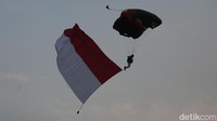 Aksi terjun payung seorang personel sambil membawa bendera Merah Putih raksasa membuat penonton terkagum-kagum.
