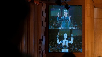 Robot yang juga memiliki wajah humanoid ini pertama-tama membungkukan badannya sebagai penghormatan kepada penonton dan langsung melaimbaikan tangannya untuk mengontrol tempo selama pertunjukan.